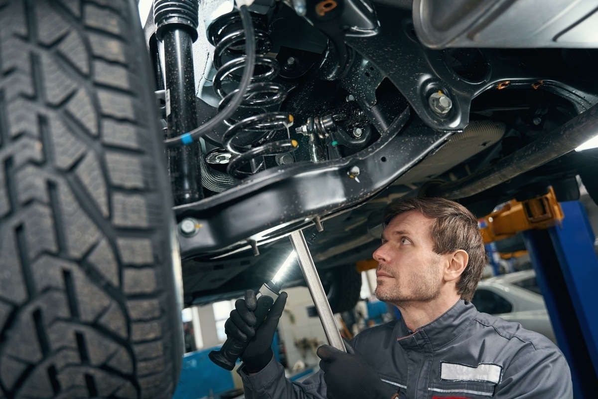 Suspension repair in Brooklyn, NY technician inspecting coil spring and shock absorber on a lifted vehicle at Cyclone Collision Center