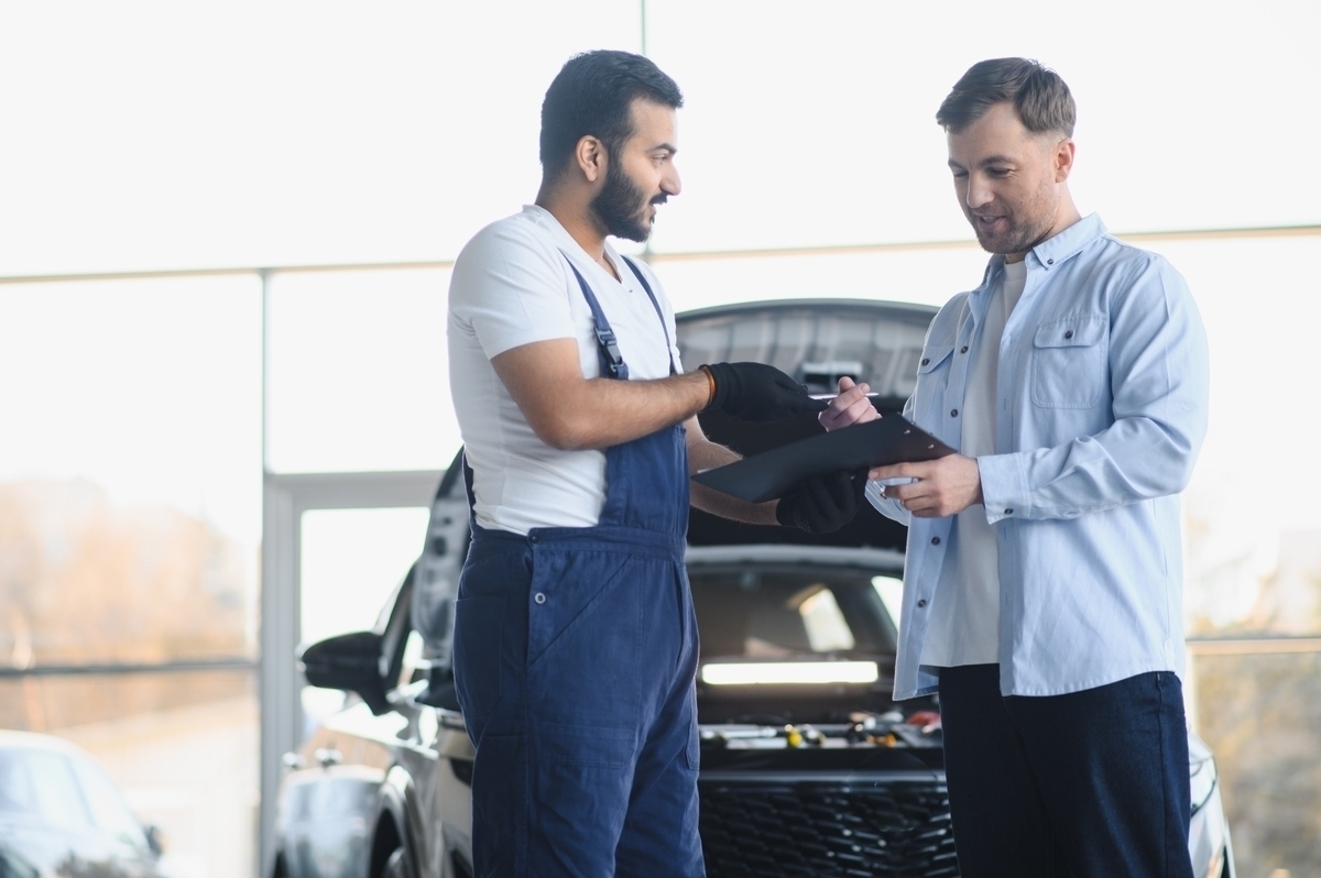Mechanic handing auto body repair warranty documents to a customer at an auto shop
