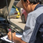Mechanic inspecting car engine with clipboard to show how car maintenance prevents towing
