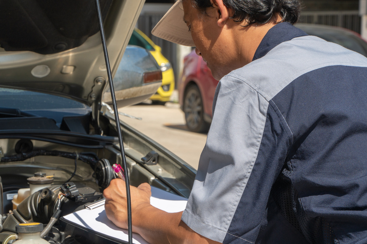 Mechanic inspecting car engine with clipboard to show how car maintenance prevents towing