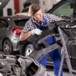 Auto body technician removing damaged bumper cover for bumper repair and replacement in a professional shop