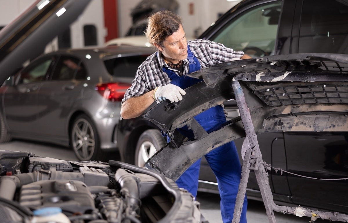 Auto body technician removing damaged bumper cover for bumper repair and replacement in a professional shop