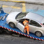 Tow truck operator accessing interior of car on flatbed illustrating concerns about personal belongings when towed