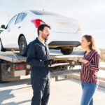 Woman questioning tow truck operator with clipboard as her car is loaded illustrating predatory towing in New York