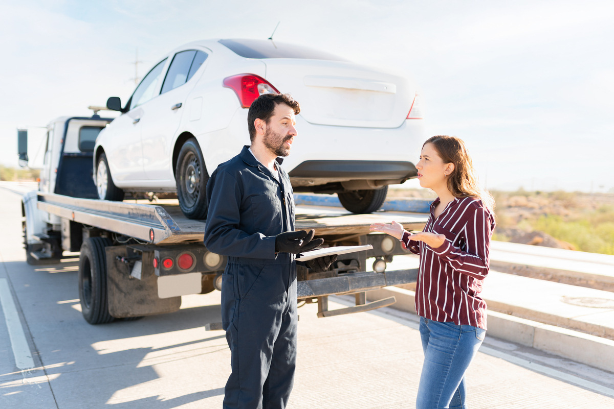 Woman questioning tow truck operator with clipboard as her car is loaded illustrating predatory towing in New York