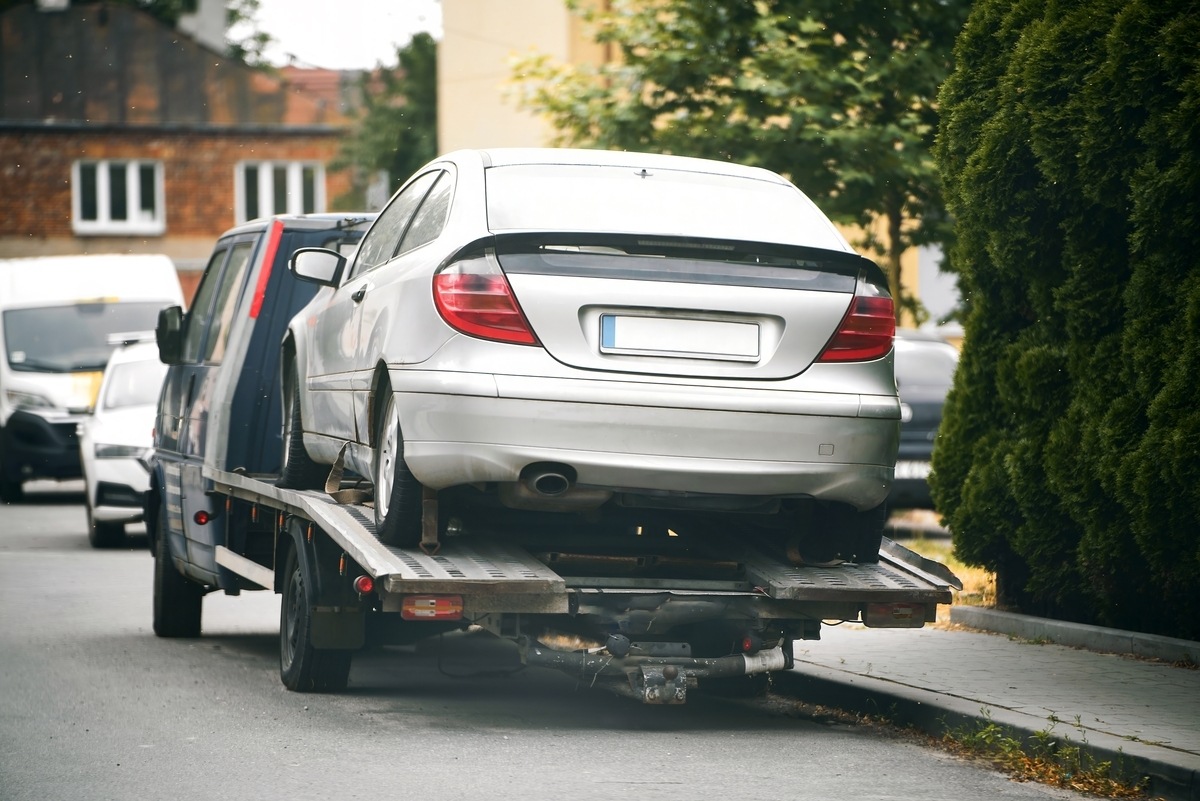 Flatbed tow truck transporting a silver sedan through a residential street for towing service in Bensonhurst