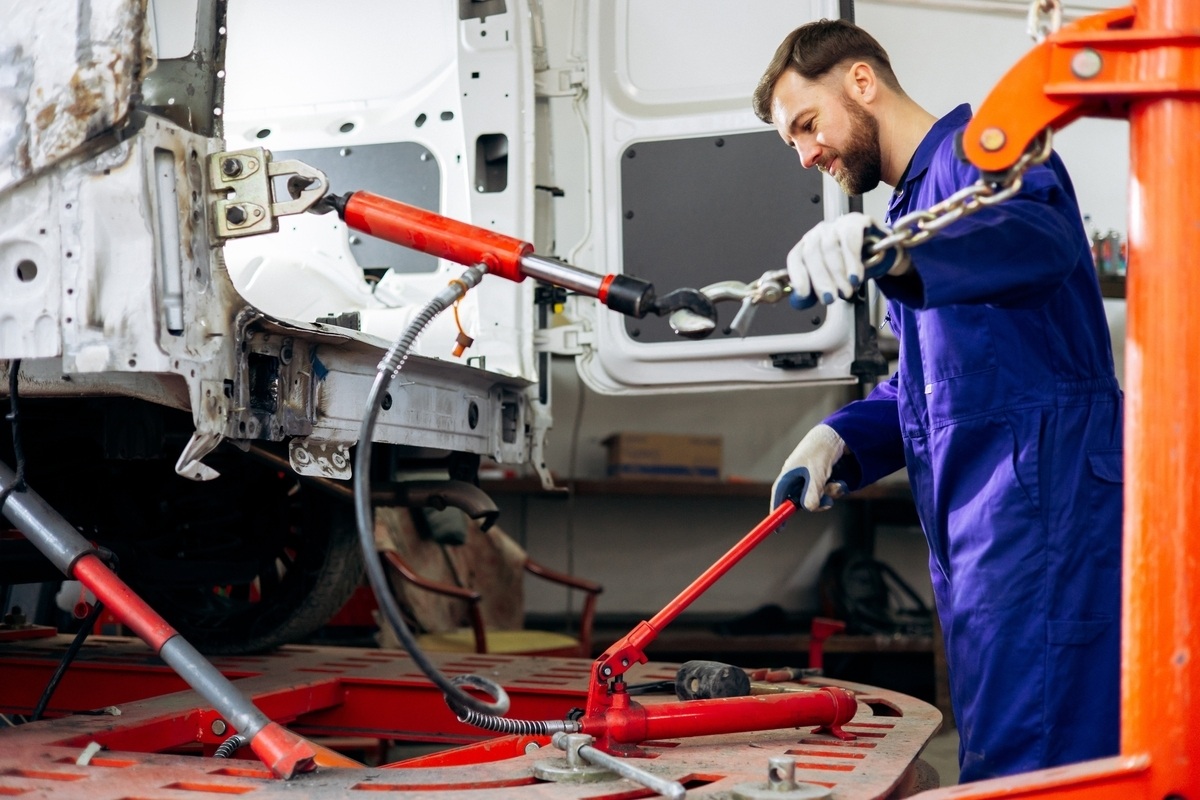 Technician using hydraulic equipment to repair unrepaired frame damage on a vehicle in an auto body shop