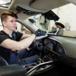 Technician working on windshield ADAS sensor during auto body shop glass replacement inside modern vehicle