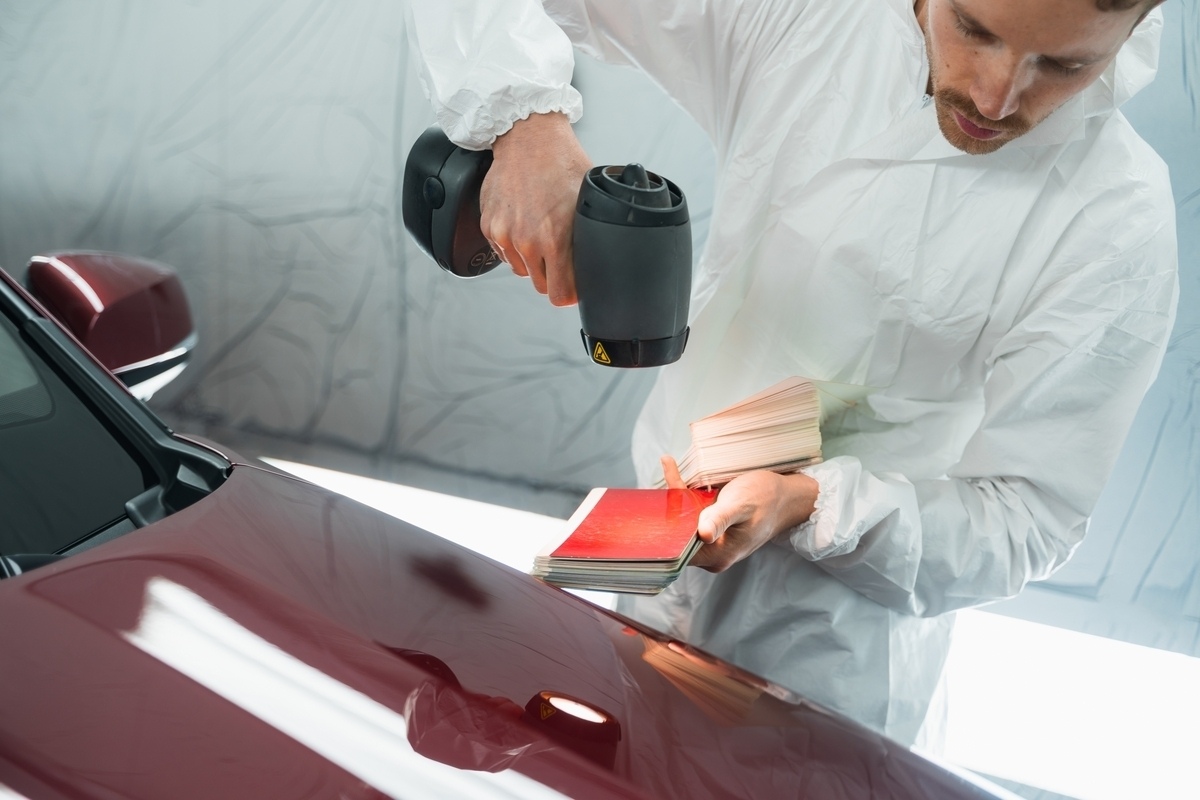 Technician using spectrophotometer on vehicle panel for auto body shop paint matching with color swatches