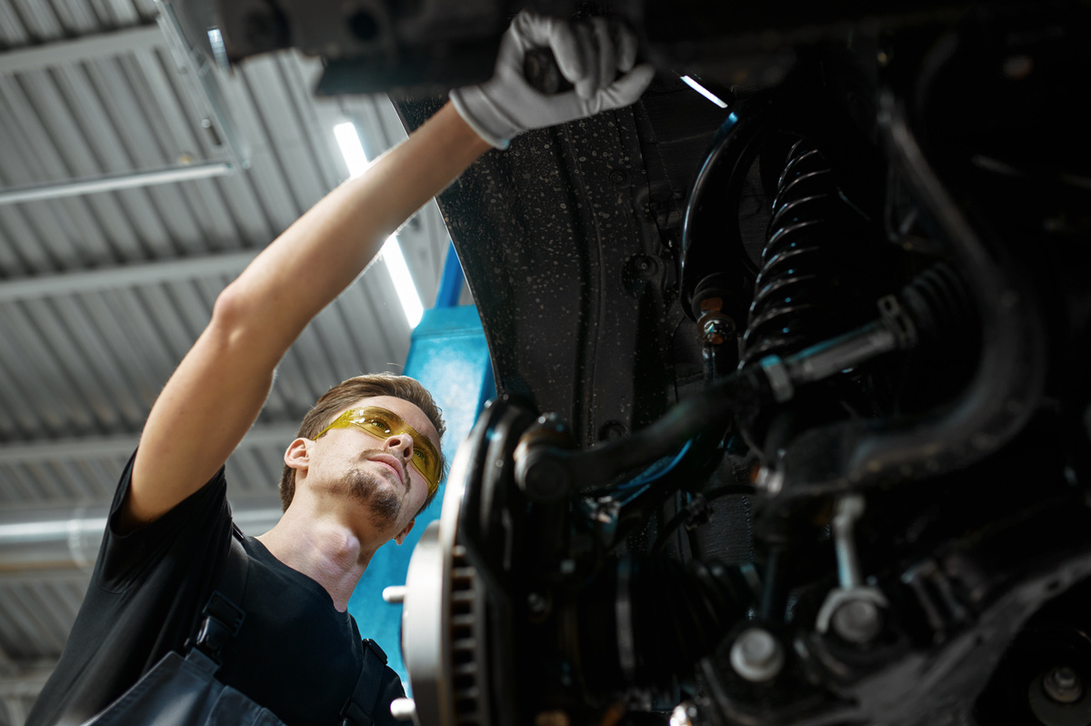 Technician inspecting suspension components under lifted vehicle for auto body shop suspension repair