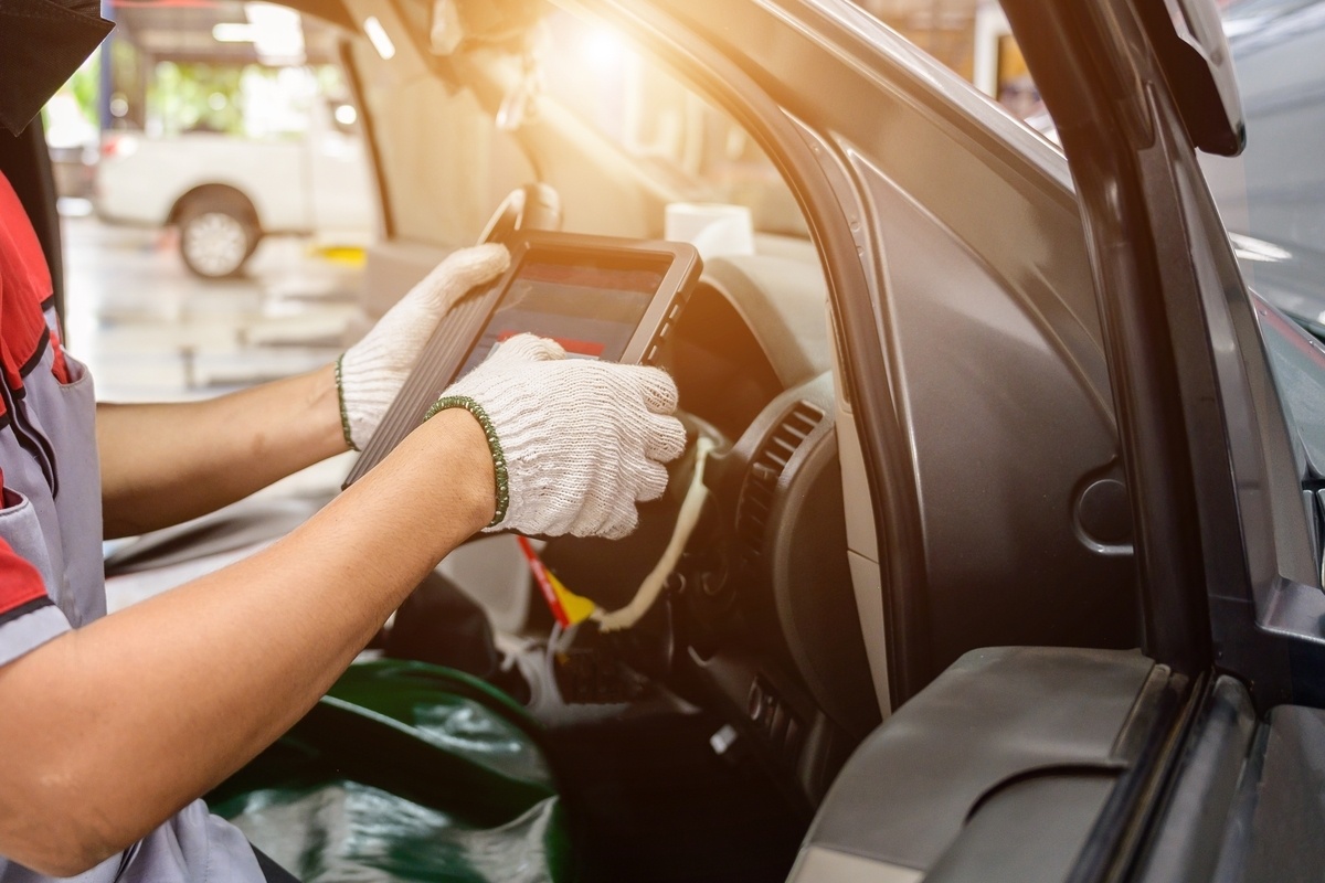 Technician using OBD diagnostic scanner inside vehicle for auto body shop electrical repair after a crash